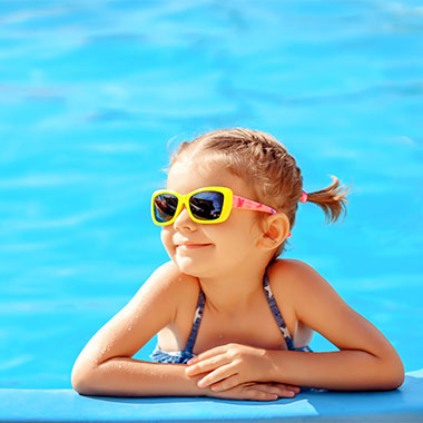 Malé dítě se usmívá na okraji bazénu. Tvrdost vody v bazénech může poškozovat povrchy bazénu a korodovat potrubí.